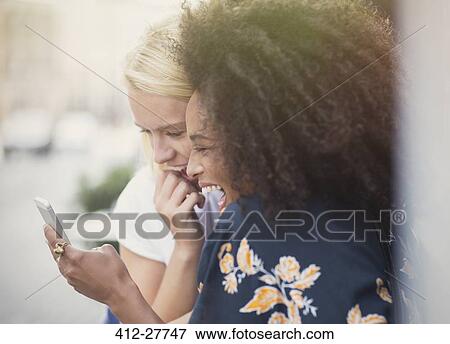 Stock Photo - Laughing friends texting with cell phone. Fotosearch