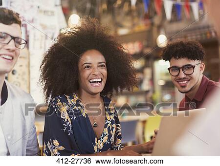 Stock Photograph - Laughing friends with laptop in cafe. Fotosearch