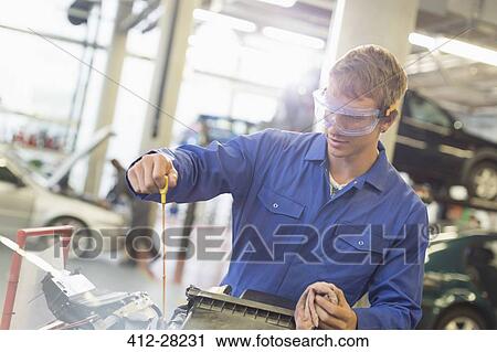 Stock Image - Mechanic checking engine oil in auto repair shop. Fotosearch