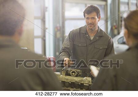 Stock Photo - Mechanic explaining engine to students in auto repair shop. Fotosearch