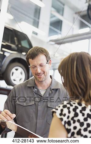 Stock Image - Mechanic with clipboard talking to customer in auto repair shop. Fotosearch