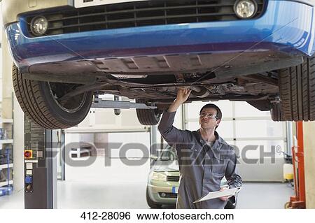 Stock Photograph - Mechanic with clipboard working under car in auto repair shop. Fotosearch