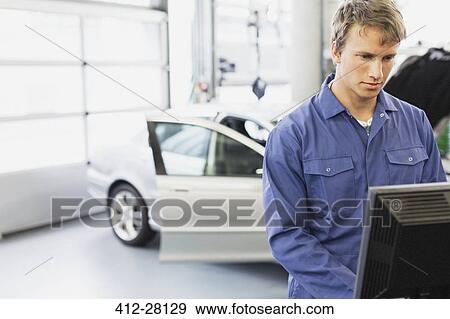 Mechanic working at computer in auto repair shop View Large Photo Image Stock Photo - Mechanic working at computer in auto repair shop. Fotosearch