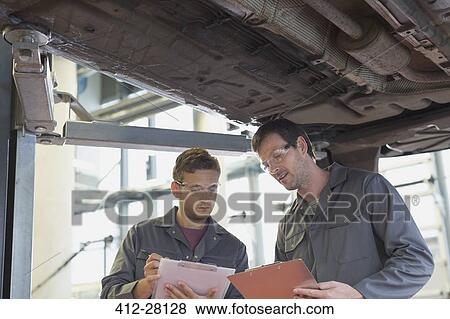 Stock Photo - Mechanics with clipboards talking under car in auto repair shop. Fotosearch