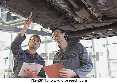Stock Image - Mechanics with clipboards working under car in auto repair shop. Fotosearch