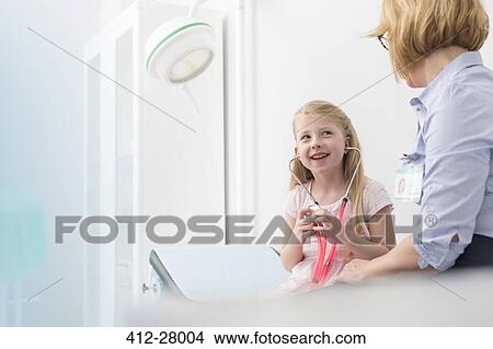 Pediatrician watching girl patient playing with stethoscope in examination room View Large Photo Image Picture - Pediatrician watching girl patient playing with stethoscope in examination room. Fotosearch