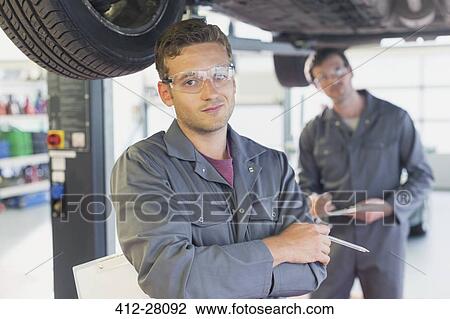 Stock Image - Portrait confident mechanic under car in auto repair shop. Fotosearch