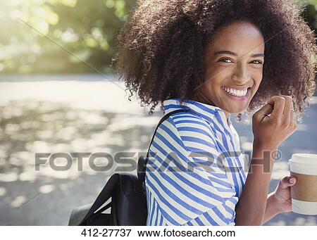 Stock Photo - Portrait enthusiastic woman with afro drinking coffee in park. Fotosearch