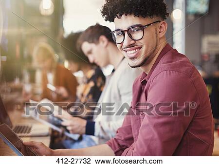 Stock Image - Portrait smiling man with curly black hair using digital tablet in cafe. Fotosearch