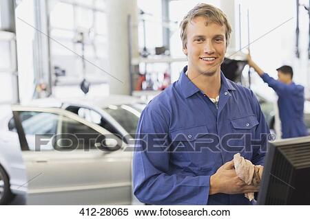Stock Photography - Portrait smiling mechanic at computer in auto repair shop. Fotosearch