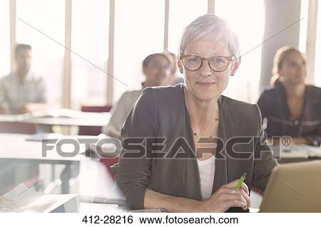 Stock Photograph - Portrait smiling senior woman at laptop in adult education classroom. Fotosearch