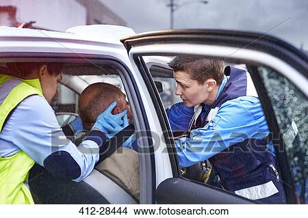 Picture - Rescue workers carefully tending to car accident victim in car. Fotosearch