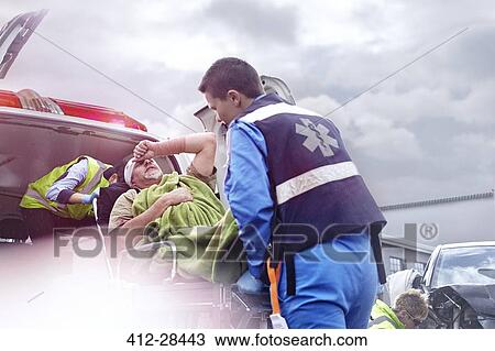 Stock Image - Rescue workers loading car accident victim into back of ambulance. Fotosearch