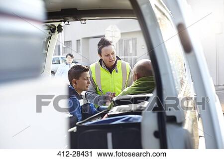 Stock Image - Rescue workers talking at back of ambulance. Fotosearch