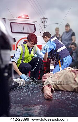 Rescue workers tending to car accident victim in road View Large Photo Image Stock Photo - Rescue workers tending to car accident victim in road. Fotosearch