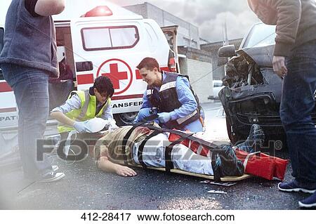 Stock Photo - Rescue workers tending to car accident victim in road. Fotosearch