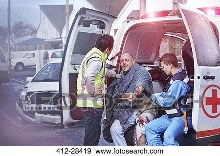 Stock Photo - Rescue workers tending to car accident victim at back of ambulance. Fotosearch