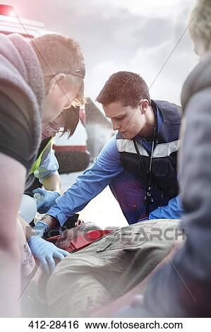 Stock Photograph - Rescue workers tending to car accident victim in road. Fotosearch
