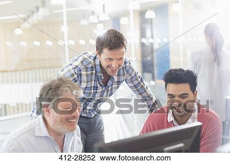 Stock Image - Smiling businessmen working at computer in office. Fotosearch
