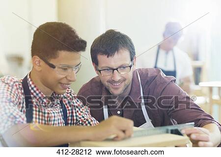Stock Image - Smiling carpenters measuring wood with ruler in workshop. Fotosearch