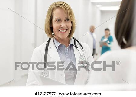 Stock Image - Smiling doctor talking to patient in hospital corridor. Fotosearch
