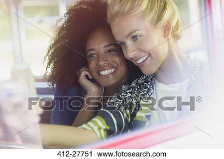 Stock Image - Smiling friends taking selfie on bus. Fotosearch