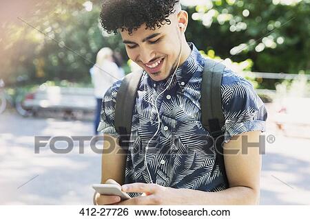 Stock Photograph - Smiling man with curly black hair listening to music with headphones and mp3 player. Fotosearch