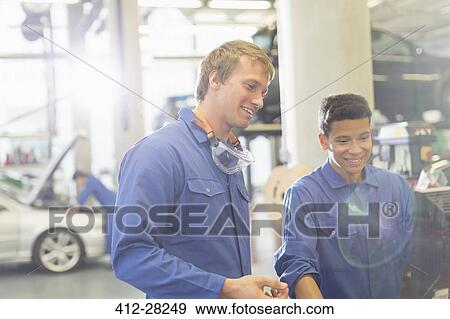 Stock Photo - Smiling mechanics using computer in auto repair shop. Fotosearch