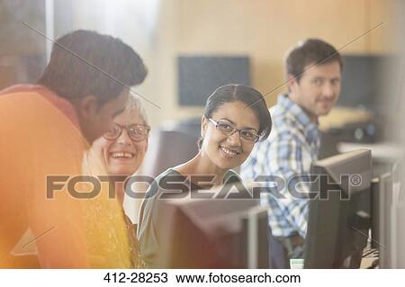 Stock Image - Smiling students talking at computers in adult education classroom. Fotosearch
