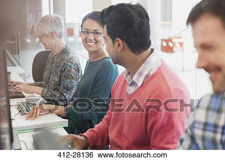 Stock Photograph - Smiling students talking at computers in adult education classroom. Fotosearch