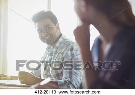 Stock Image - Smiling students talking in adult education classroom. Fotosearch