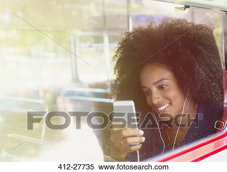 Stock Photography - Smiling woman with afro listening to music with headphones and mp3 player on bus. Fotosearch