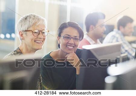 Picture - Smiling women at computer in adult education classroom. Fotosearch
