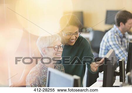 Stock Photography - Smiling women talking at computer in adult education classroom. Fotosearch