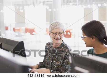 Stock Photography - Smiling women talking at computers in adult education classroom. Fotosearch