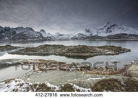 Snow covered mountain range behind craggy bay, Sund, Lofoten Islands, Norway View Large Photo Image Stock Photograph - Snow covered mountain range behind craggy bay, Sund, Lofoten Islands, Norway. Fotosearch