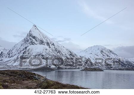 Stock Image - Snow covered mountains along cold lake, Lofoten Islands, Norway. Fotosearch