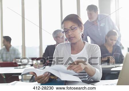 Stock Image - Student reading textbook in adult education classroom. Fotosearch