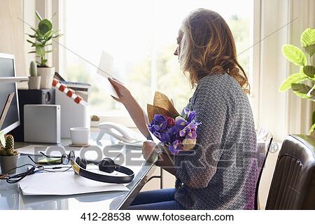Stock Photo - Woman receiving flower bouquet and reading card in home office. Fotosearch