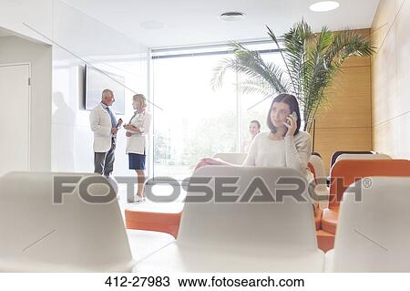 Stock Image - Woman talking on cell phone in hospital lobby. Fotosearch