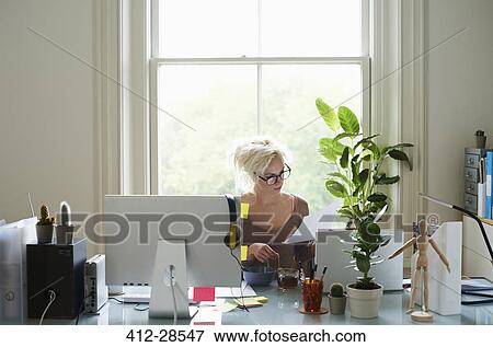 Young woman reading paperwork at desk in home office View Large Photo Image Stock Photo - Young woman reading paperwork at desk in home office. Fotosearch