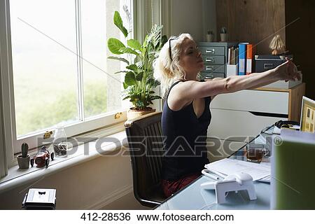 Young woman stretching arms at desk in home office View Large Photo Image Stock Photograph - Young woman stretching arms at desk in home office. Fotosearch