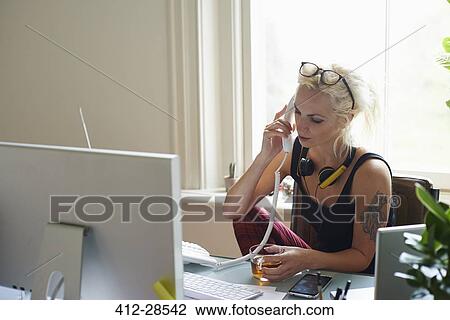 Young woman with headphones and tattoo drinking tea and talking on telephone in home office View Large Photo Image Stock Image - Young woman with headphones and tattoo drinking tea and talking on telephone in home office. Fotosearch
