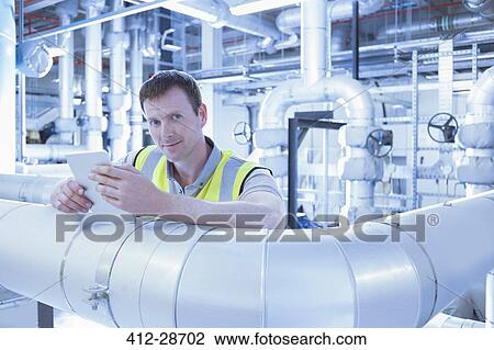 Stock Image - Portrait confident worker with digital tablet leaning on pipe in factory. Fotosearch