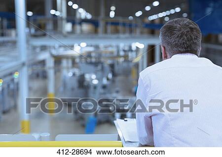 Picture - Supervisor with clipboard on platform overlooking factory. Fotosearch
