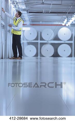 Picture - Worker examining large paper spools in printing plant. Fotosearch