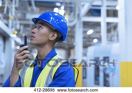 Stock Photography - Worker in hard-hat using walkie-talkie in factory. Fotosearch