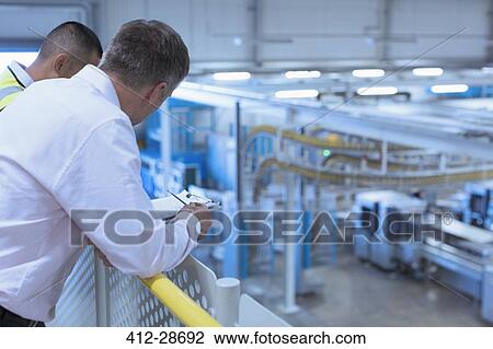 Stock Image - Workers leaning on railing overlooking factory. Fotosearch