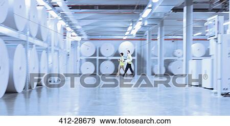 Stock Photo - Workers walking along large paper spools in printing plant. Fotosearch