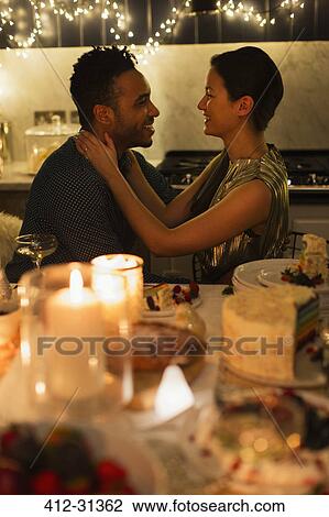 Stock Image - Affectionate couple at candlelight Christmas dinner. Fotosearch